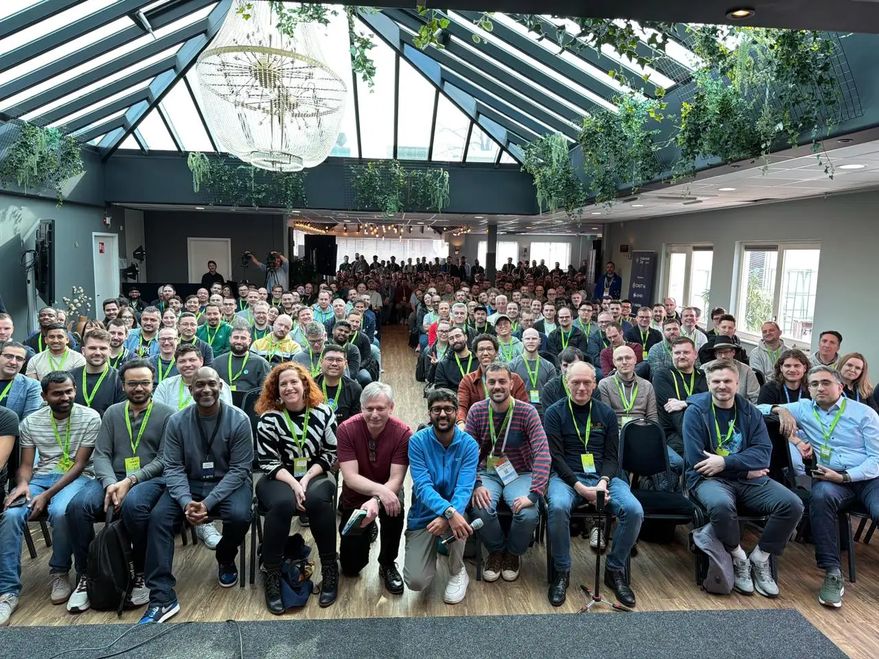 A packed glasshouse venue at KubeAuto Day Amsterdam, hundreds of attendees seated for the group photo with Kunal at the front.