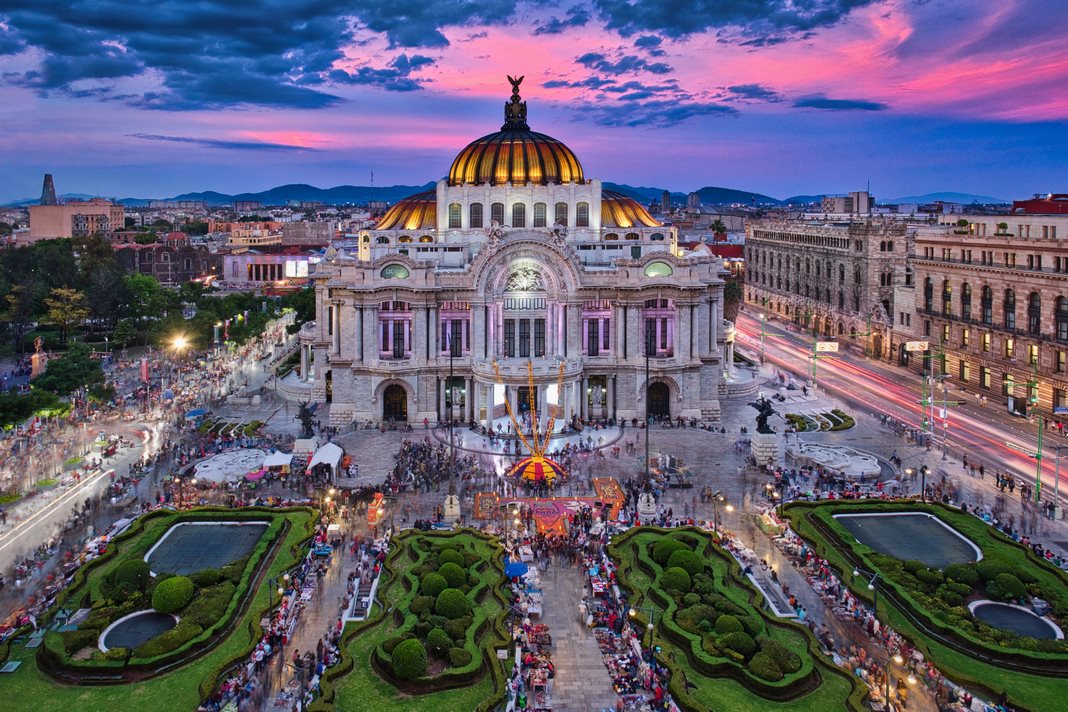 The Palacio de Bellas Artes in Mexico City at dusk, its domes lit under a pink sky