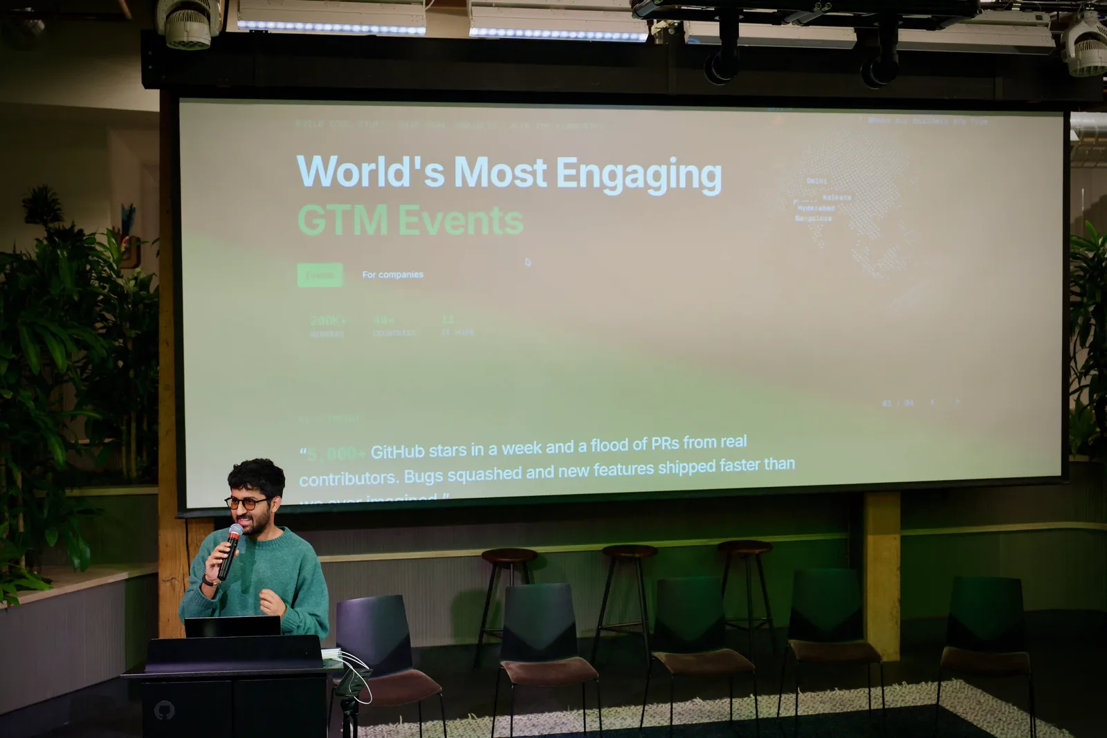 A host speaking into a microphone at a lectern in front of a projected WeMakeDevs slide reading World's Most Engaging GTM Events